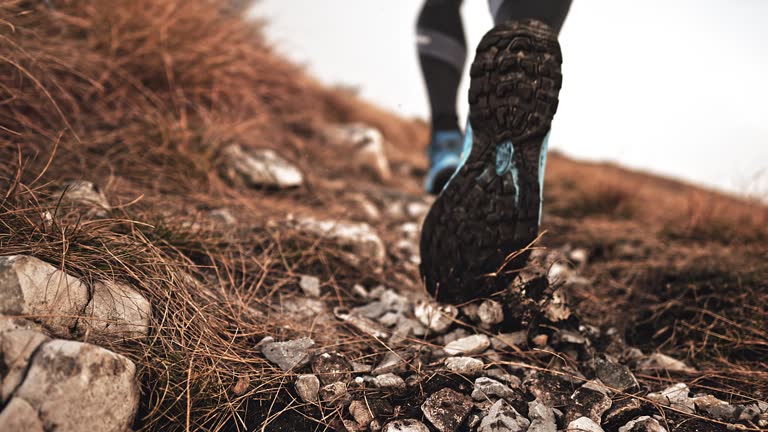 SLO MO Legs of a male runner running uphill and kicking gravel into the air