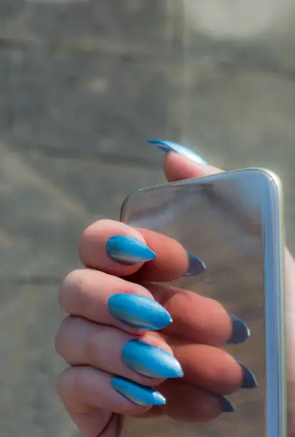 Woman is showing her Baby blue stiletto nails reflected in her smartphone