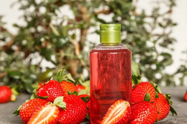 Natural cosmetics ingredients, for a body and hair from strawberry. Red liquid in a transparent bottle. Strawberry oil, shampoo, shower gel. A mask for hair