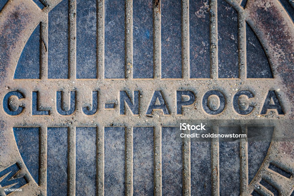 Close up of manhole cover with words 'Cluj Napoca', Romania Close up color image depicting a drain, or manhole, cover on the street in the city of Cluj Napoca, in the Transylvania region of Romania. The drain cover has the name of the city - Cluj Napoca - written on it in large bold lettering. Room for copy space. Cluj Napoca - Romania Stock Photo