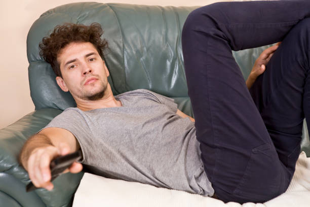 istock Lazy man with the remote on the couch 957693784