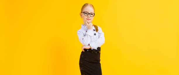Girl with red hair on a yellow background. A charming girl in transparent glasses put a finger to her chin. Portrait of a beautiful girl in a white blouse and black skirt. see through leggings stock pictures, royalty-free photos & images