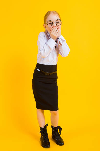 Girl with red hair on a yellow background. A charming girl in transparent glasses laughs and covers her mouth with her hands. Portrait of a beautiful girl in a white blouse and black skirt. see through leggings stock pictures, royalty-free photos & images