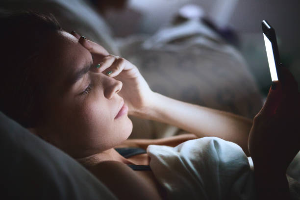 Woman in bed with smartphone Tired woman in bed with smartphone, low light woman sleeping in bed at night stock pictures, royalty-free photos & images