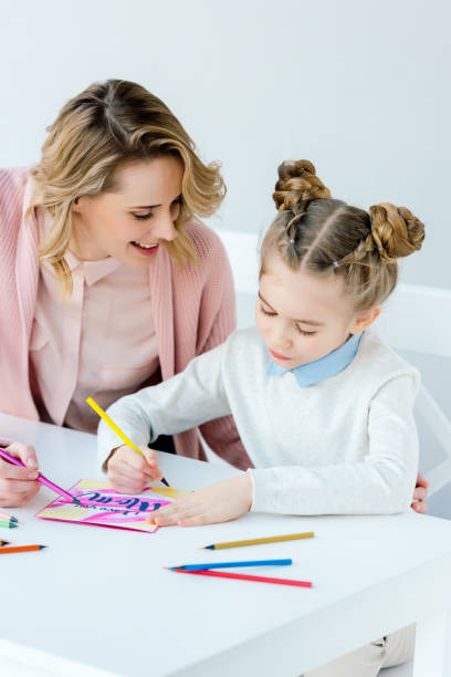 istock cheerful mother and daughter making greeting postcard together at table 957703352