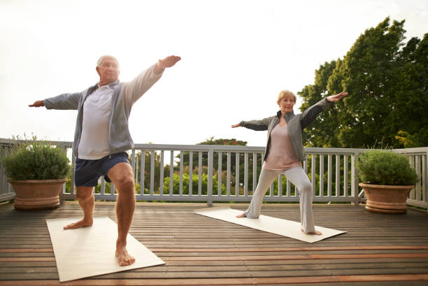 Yoga keeps us young Shot of a senior married couple practicing yoga at home warrior position stock pictures, royalty-free photos & images