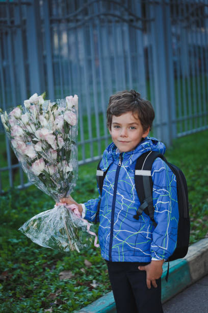 istock Elementary school pupil with a backpack behind his back and a bouquet of flowers. 957709614
