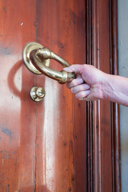 istock man pulls on brass door knocker, on wooden wooden door 957736408