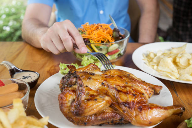 A man holding a fork is eating a grilled chicken.