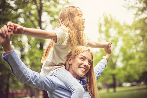 Mother carrying daughter on shoulders and spending time in park.