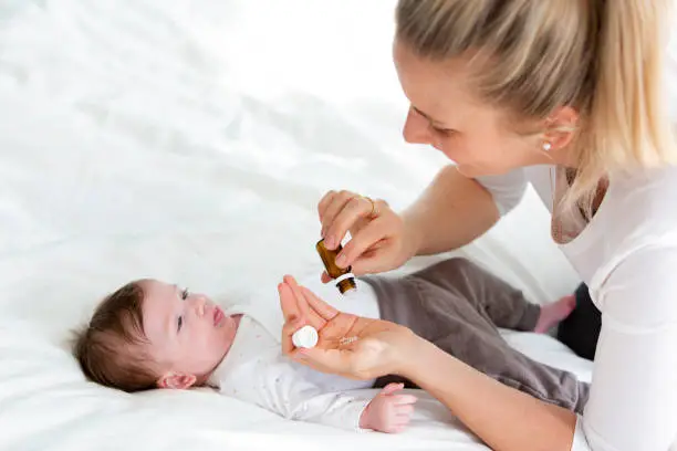 beautiful young mother is giving her cute baby daughter homeopathic globules