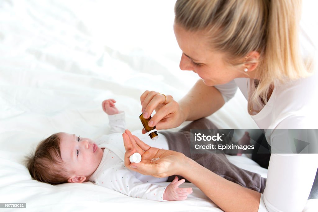 beautiful young mother is giving her cute baby daughter homeopathic globules Homeopathic Medicine Stock Photo