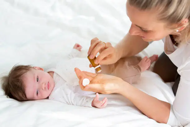 beautiful young mother is giving her cute baby daughter homeopathic globules