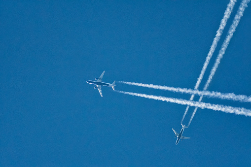 Looking up at a pair commercial passenger jets flying at a high altitude with their vapor trails intersecting against the blue sky. Concept - Crowed skies