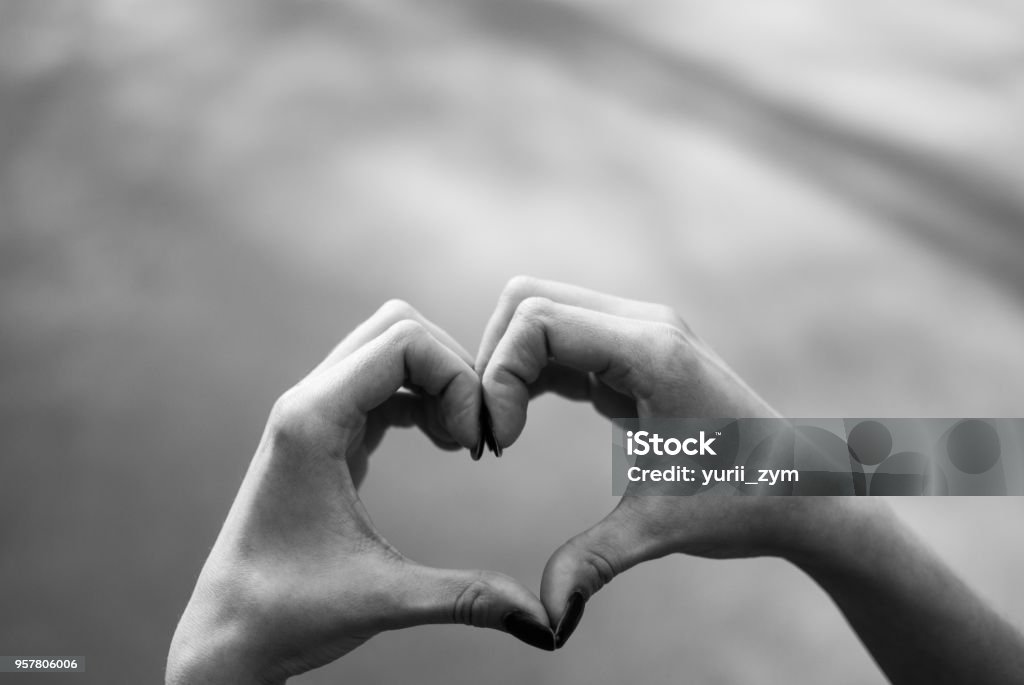 Girl making a heart shape gesture against grey asphalt background. Girl making a heart shape gesture against grey asphalt background. Black and white Heart Shape Stock Photo