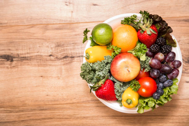 sanos frutas y verduras en un tazón sobre fondo de madera - tazón para frutas fotografías e imágenes de stock