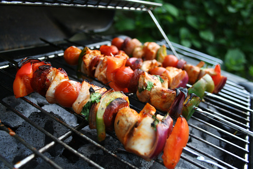 several chicken kebabs on skewers cooking on a barbecue