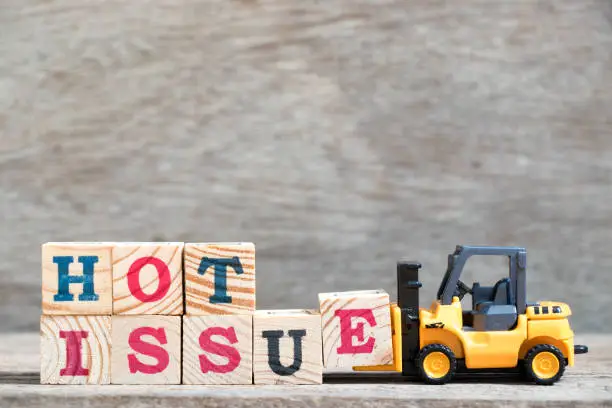 Photo of Toy forklift hold letter block e to complete word hot issue on wood background