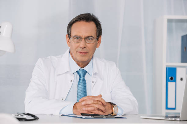 istock handsome doctor sitting at working table and looking at camera 957834234