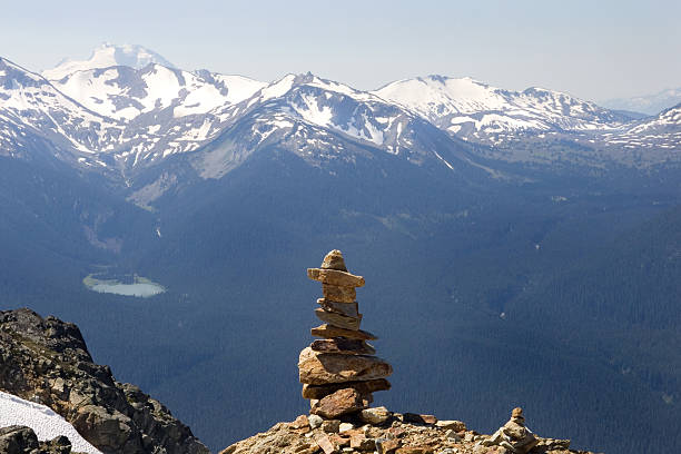 Nature's Silent Admirer View at the top of Whistler Mountain.  Mother nature's peaks in the background, and a Manmade one- Inukshuk in the foreground..  inukshuk whistler cairn mountain stock pictures, royalty-free photos & images