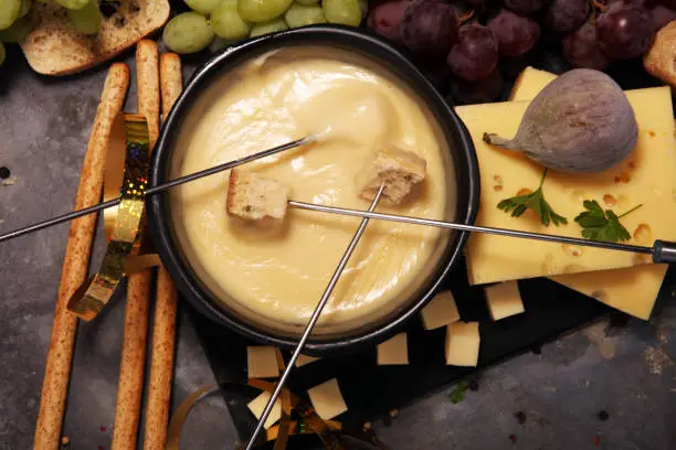 Gourmet Swiss fondue dinner on a winter evening with assorted cheeses on a board alongside a heated pot of cheese fondue with two forks dipping bread