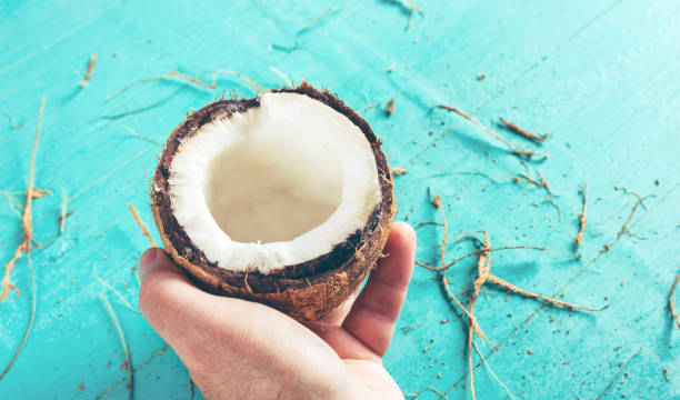 istock Half of a chopped coconut in a hand on a blue background 957852156