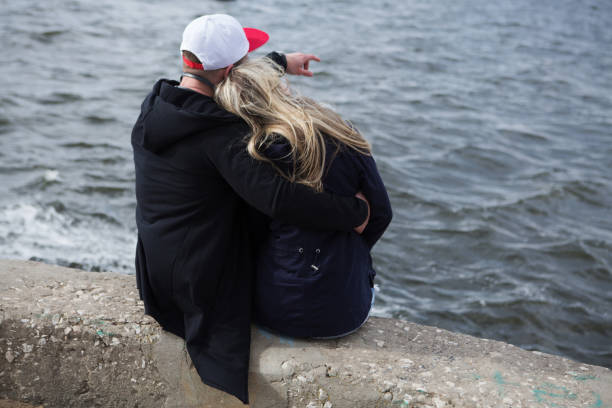 istock couple embraces sitting the coast, rear view 957859212