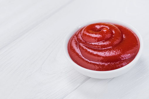 Bowl of ketchup or tomato sauce on a white wooden table