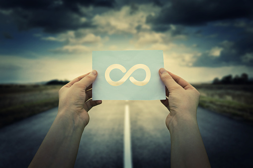 Close up of woman hands holding a paper sheet with infinite sign inside, over endless asphalt road background. The infinity way to nowhere, business confusion concept.