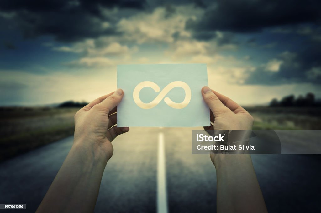 business confusion Close up of woman hands holding a paper sheet with infinite sign inside, over endless asphalt road background. The infinity way to nowhere, business confusion concept. Infinity Stock Photo