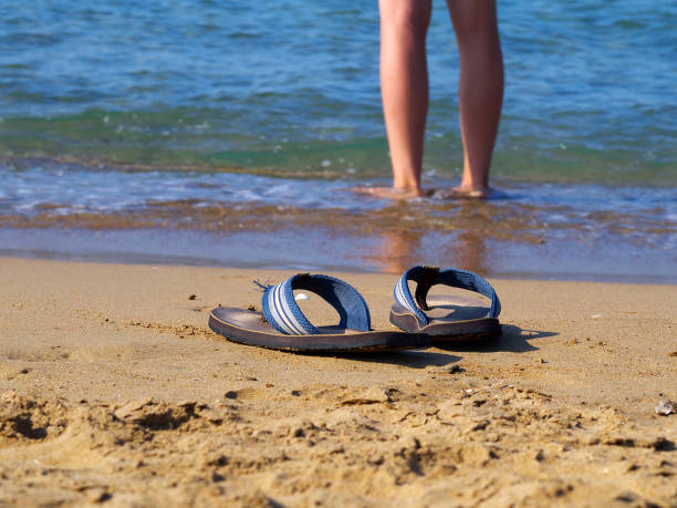istock flippers on sand and man walking in water in background, 957872540