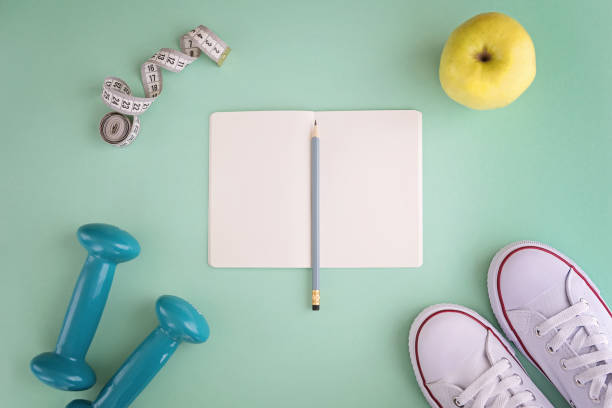 istock White sneakers, notebook, dumbbells, apple and tape measure on mint background 957876476