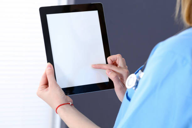 istock Woman doctor using tablet computer while standing straight in hospital office, closeup. Healthcare, insurance and medicine concept 957879346