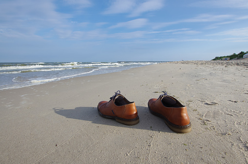 Holiday concept reflected by businessman shoes left on the beach.