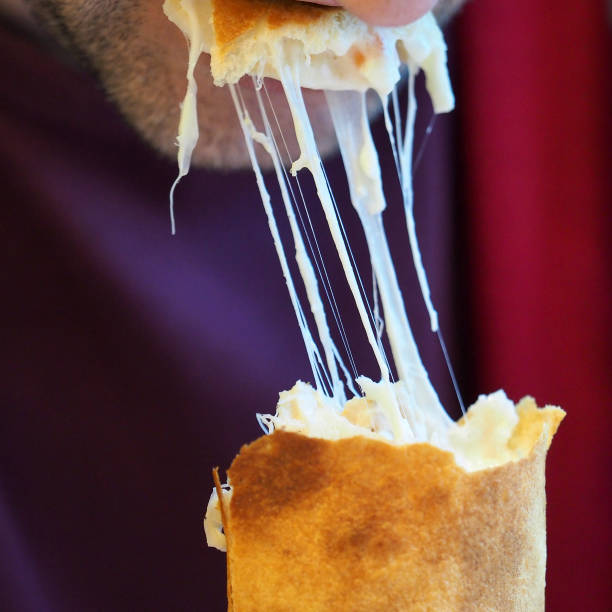 A man eats a burrito from a thin wheat cake with meat stuffing, fresh vegetables, sauce and Mozzarella cheese. Melting cheese