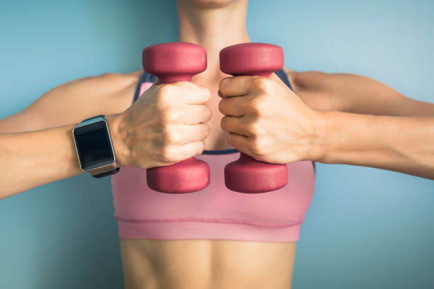 Fit girl holding weights and wearing smartwatch. Fitness and technology concept. woman weight training stock pictures, royalty-free photos & images