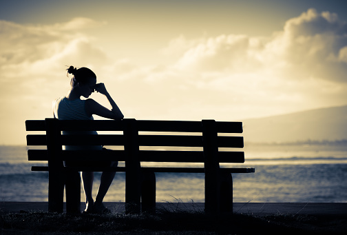 Sad and lonely woman sitting alone on a park bench.