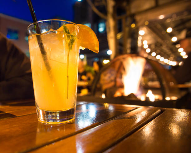 Cocktail outside at night Refreshing cocktail beverage with ice and straw scene from outdoor restaurant at night with lights and firepit. drinks on the deck stock pictures, royalty-free photos & images