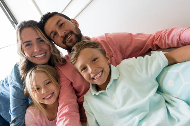 pretty latin american family relaxing inside their flat taking a selfie looking at camera with a toothy smile - offspring child toothy smile beautiful imagens e fotografias de stock