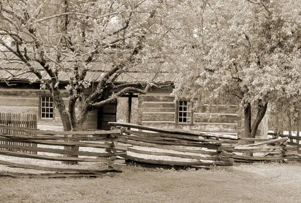 Split rail fence surrounding a log cabin shelter. Sepia-toned image.