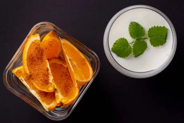 fresh orange slices with cinnamon in a glass bowl and white color drink in a glass with