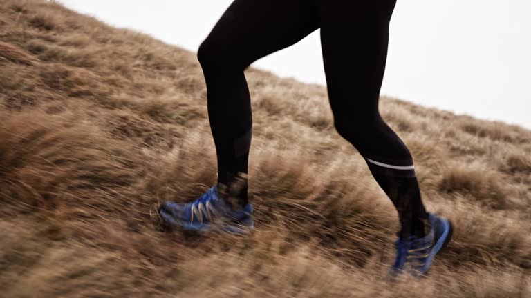 SLO MO TS Legs of a male runner ascending a mountain on a grassy slope