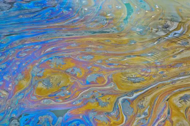 An environmental concern in a Texas bayou as a film of colorful oily pollutants cover the rippling, stagnant water. This can be the result of illegal dumping or factory runoff.