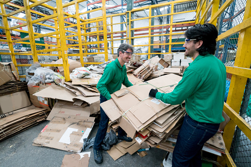 Team of people working in a recycling factory sorting cardboard boxes and looking very happy - environmental concepts