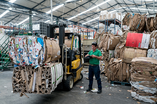 Portrait of a happy man working in a recycling factory sorting the garbage using a forklift - environmental concepts