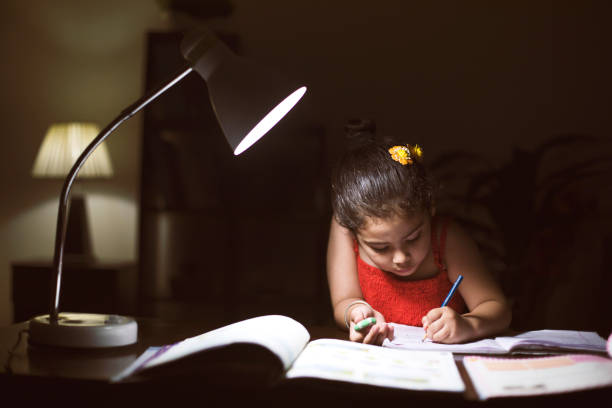 Girl doing homework at home Little girl doing homework in book at home turning on lamp stock pictures, royalty-free photos & images