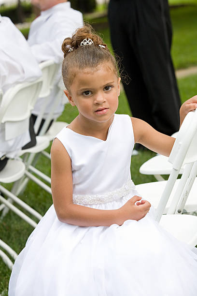 Cute little girl in white dress holding ranunculus flowers bouquet on birthday party. Little flower girl at wedding. Child with summer flowers. Kid with spring blossoms on christening celebration.