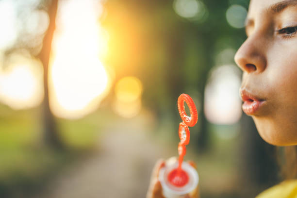 Cute little girl having fun and blowing soap bubbles outdoors