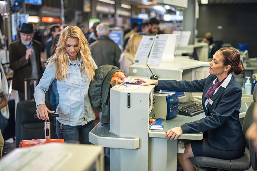 Blond woman checking in her luggage and handing over passport at an airport check-in counter