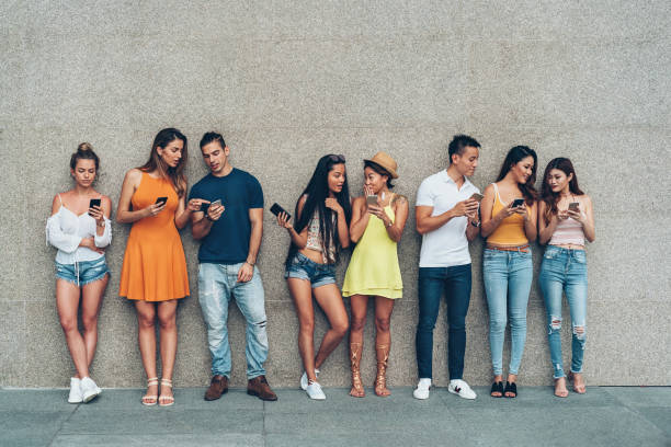 Digital generation Group of young people with smart phones standing in a row outdoors against a wall digital native stock pictures, royalty-free photos & images